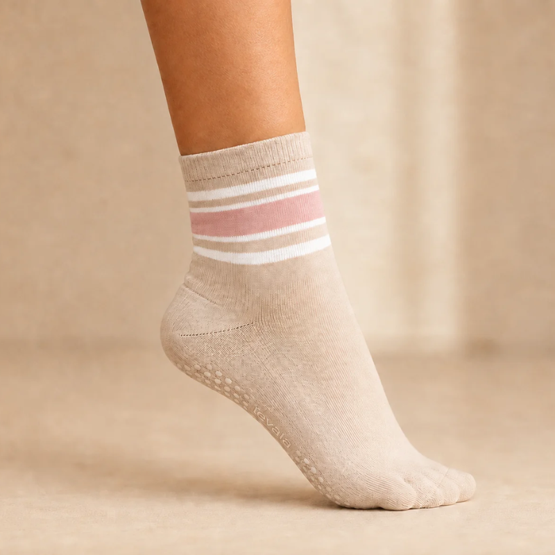 Foot wearing a levaïa Pilates Grip Sock in Blush, with pink and white ankle stripes and grip dots visible beneath the raised heel.