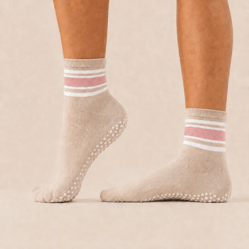 Side view of feet wearing levaïa Pilates Grip Socks in Blush, with pink and white ankle stripes and one heel raised to show grip dots.