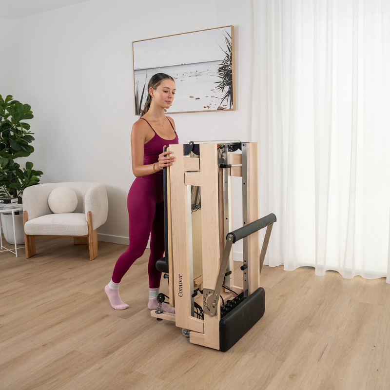 Woman standing next to a folded Lifespan Fitness Contour Folding Wooden Pilates Reformer Machine