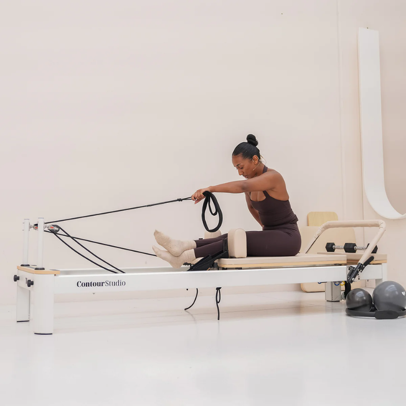 Woman using the Lifespan Fitness Contour Studio Commercial Reformer Pilates Machine in Beige inside a studio