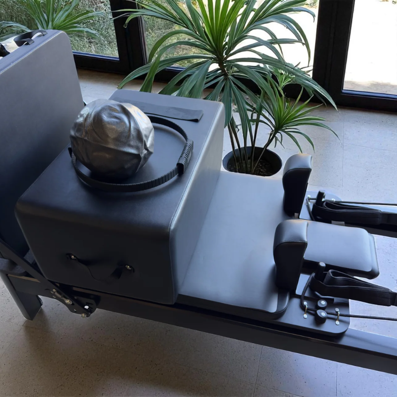 Essentials kit including Pilates ring, Pilates ball and resistance band sitting on Milaron Pearl V3 Studio Pilates Reformer Machine in Noir