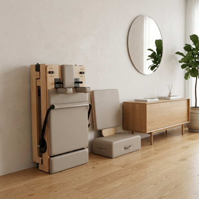 Reformys Cloud Hydraulic-Assisted Folding Pilates Reformer Machine in Beige in a folded position leaned against a wall inside a home lounge