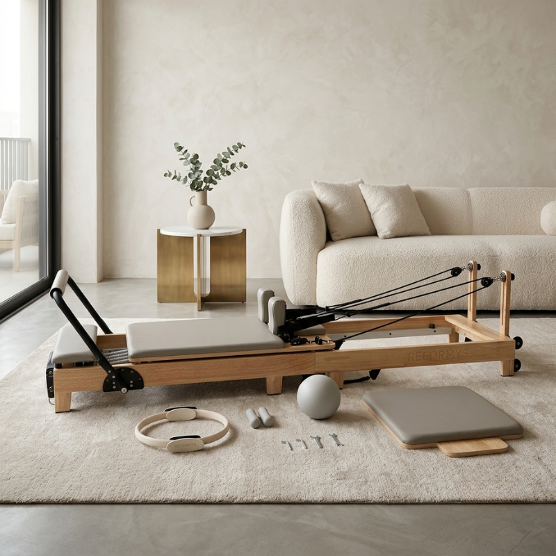 Reformys Cloud Hydraulic-Assisted Folding Pilates Reformer Machine in Beige and all its accessories laid out on the floor inside a home lounge