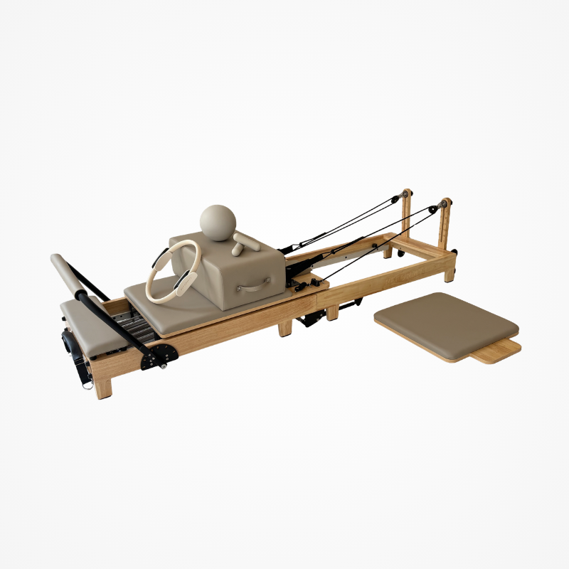 Front left angled view of Reformys Cloud Portable Pilates Reformer in Beige with jumpboard sitting next to it and rest of Pilates accessories on carriage bed