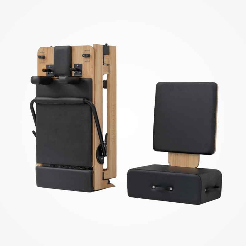 Reformys Cloud Foldable Reformer in Black folded up with jumpboard and Pilates sitting box next to it.