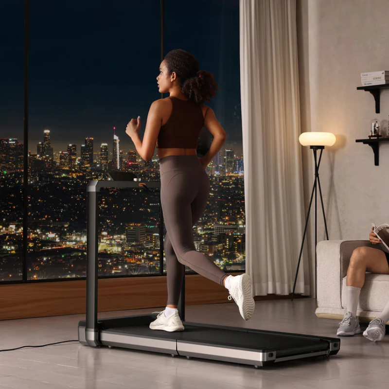Woman running on the WalkingPad MX16 Double-Fold Treadmill in a modern living room with a cityscape view at night