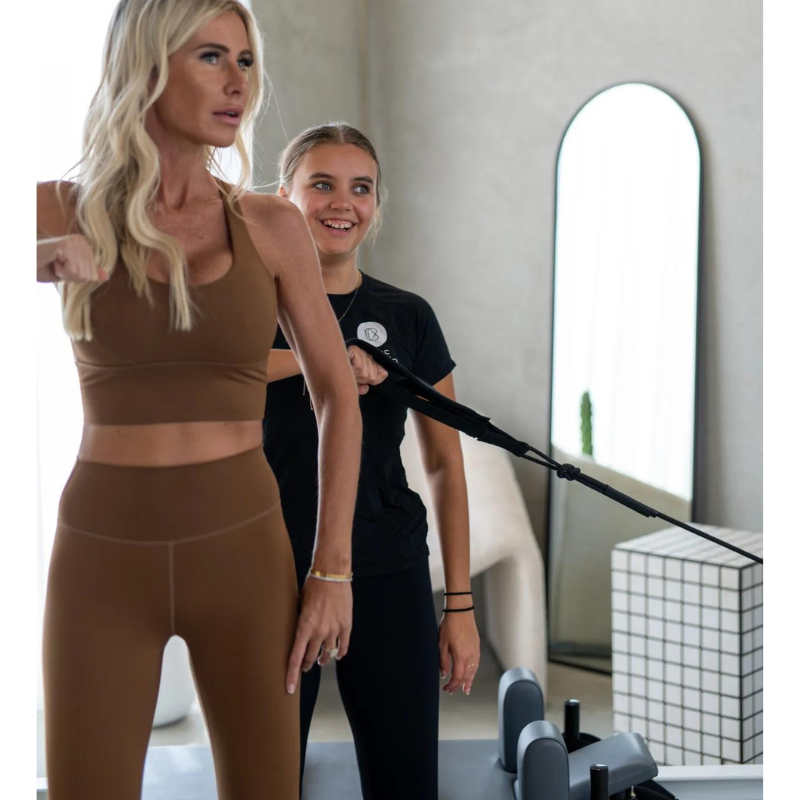 Woman Instructing Another Woman to Use Core Collab Queen Reformer with Half Trapeze