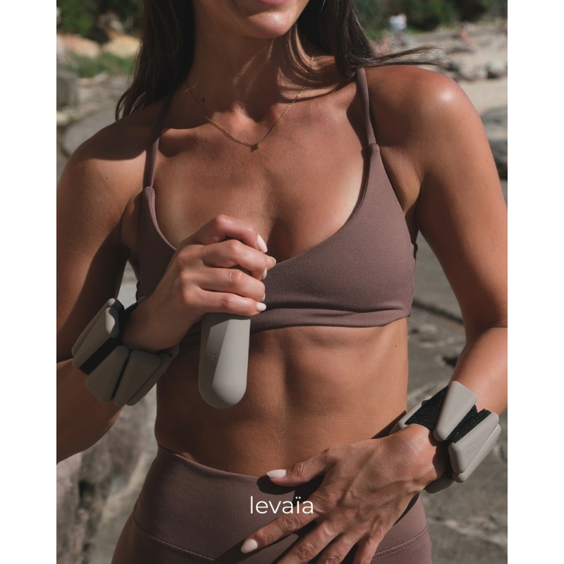Woman in workout gear at the beach holding a levaïa lifts - Handheld Pilates Weight in Taupe