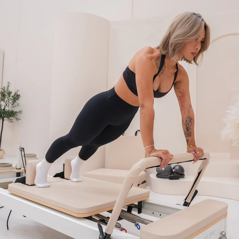 Woman exercising on the foot bar of Lifespan Fitness Contour Studio Commercial Pilates Machine in Beige inside a studio.
