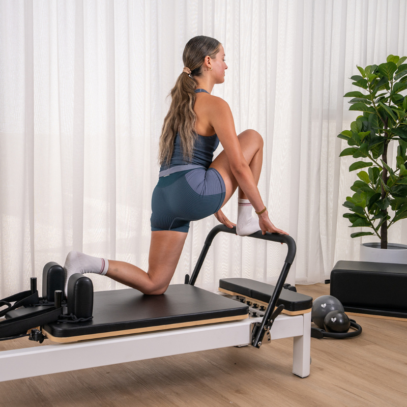 Woman exercising on the footbar and carriage of Lifespan Fitness Contour Studio Commercial Pilates Reformer Machine