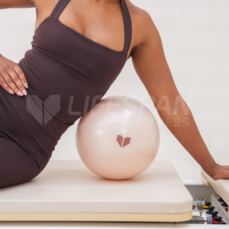 Woman sitting over a Lifespan Fitness Pilates Ball in Seashell colour on a Pilates reformer