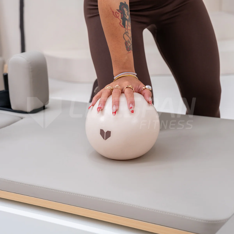 Woman holding a Lifespan Fitness Pilates Ball placed on a Pilates reformer