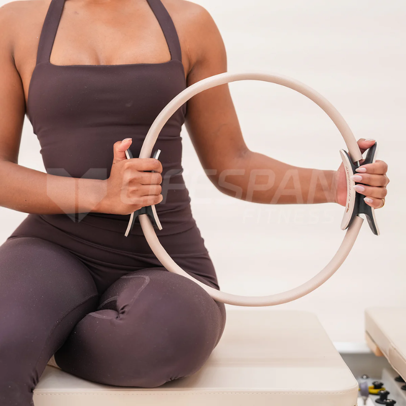 Woman holding the Lifespan Fitness Pilates Ring in Seashell colour on a Pilates reformer