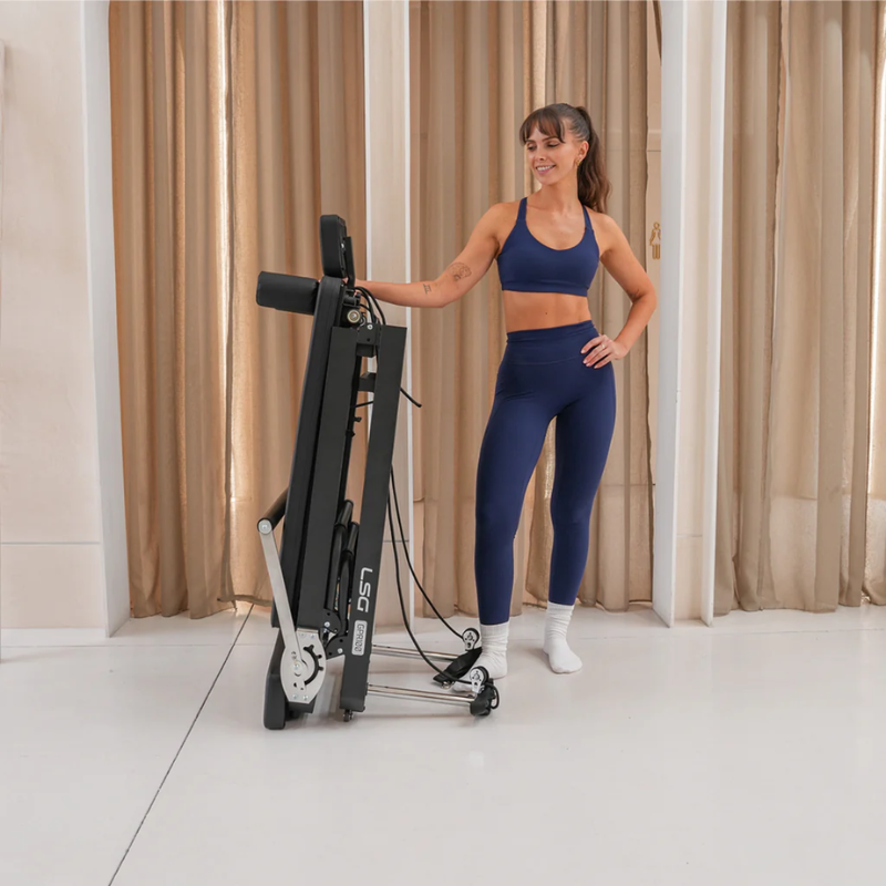 Woman standing next to the LSG GPR100 Foldable Reformer Pilates Machine in a folded upright position