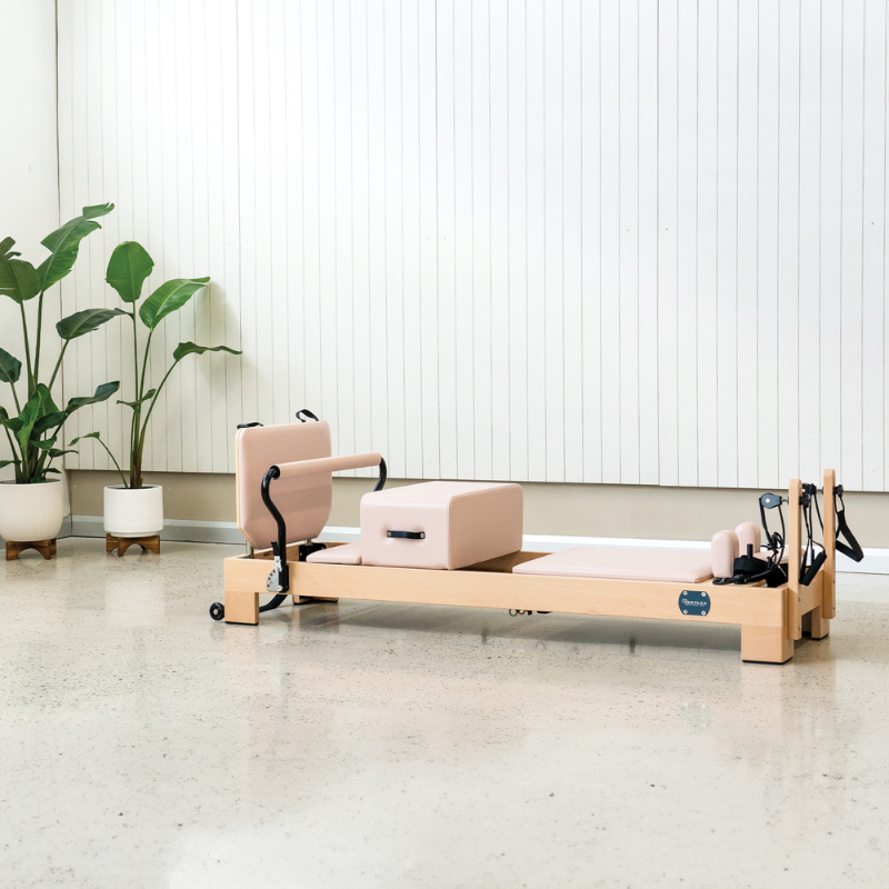Reeplex Luna Beechwood Pilates Reformer in Pink colour inside a modern studio with plants decor on the side.