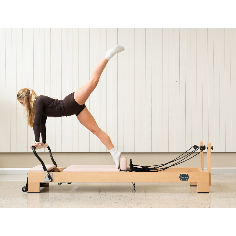 Woman doing the arabesque on the Reeplex Luna Beechwood Pilates Reformer Machine.