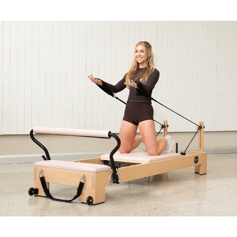 Woman doing arm work while kneeling on the Reeplex Luna Beechwood Pilates Reformer Machine.