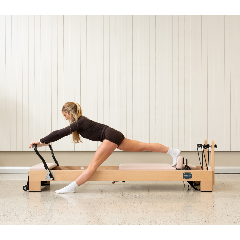 Woman doing a lunge stretch on the Reeplex Luna Beechwood Pilates Reformer Machine inside a studio.