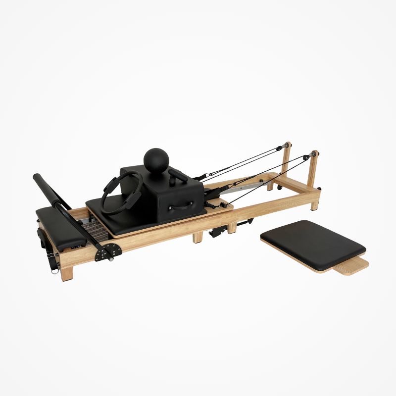 Left front view of the Reformys Cloud Folding Pilates Reformer in Black with accessories on the carriage and jumpboard on the floor next to it