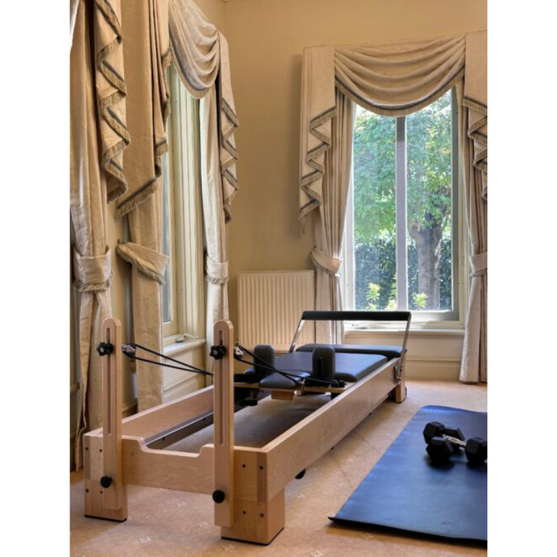 Volt Q2 Maple Wood Studio Pilates Reformer in a home gym next to exercise mat and dumbells