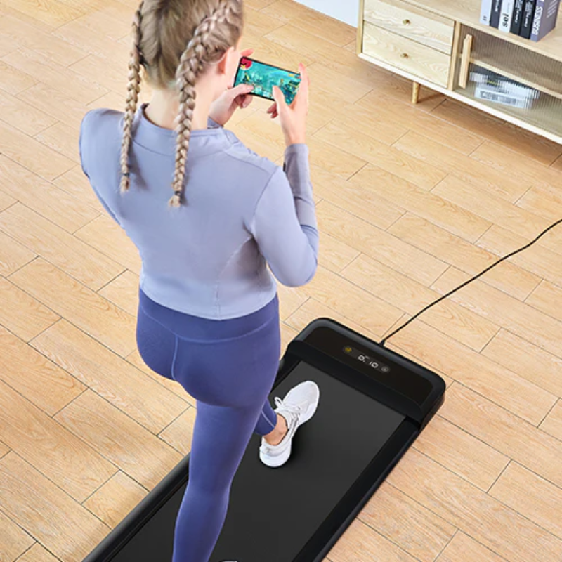 A woman looking at her phone while walking on the WalkingPad C2 Compact Folding Treadmill