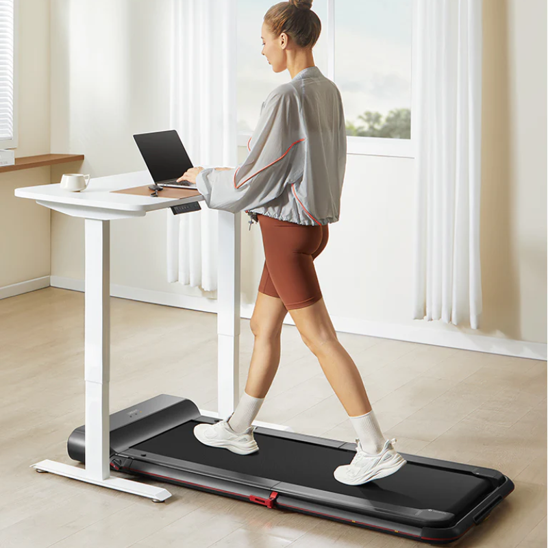 A woman working on her stand-up desk while walking on the WalkingPad R1 Pro Foldable Treadmill